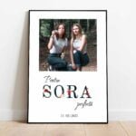 Tablou cu o fotografie cu două femei, încadrată într-o formă dreptunghiulară, textul "Pentru SORA perfectă" și o dată, ramă neagră.